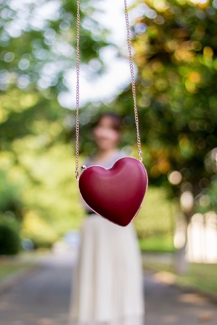 A vivid red heart-shaped pendant hanging with blurred background of a woman outdoors.